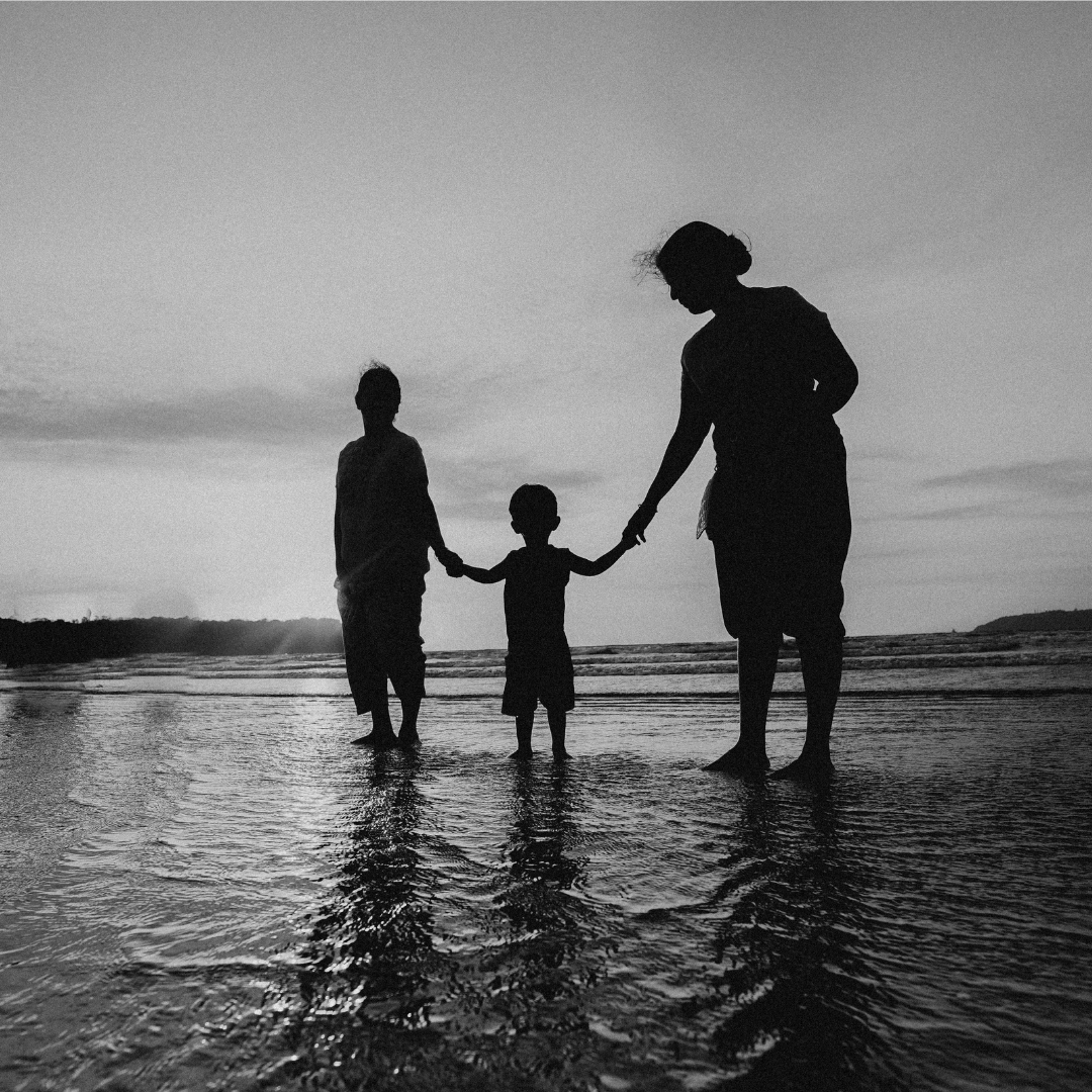 Family of three holding hands standing in water